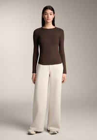 Brown long-sleeve top with a fitted design and ribbed texture, paired with high-waisted, wide-leg white pants. Neutral sneakers complete the look.