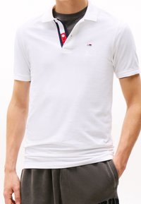 Vit pikétröja i bomull med korta ärmar, med en kontrasterande randig krage och en liten logotyp på bröstet.