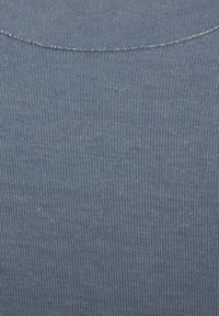 Nahaufnahme von blauer gerippter Stoff mit einem ausgefransten Nahtrand und zwei kleinen Löchern in der Nähe der unteren linken Ecke.