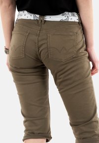 Pantalons cropped en khaki avec poches arrière présentant une couture courbée. Le tissu est lisse, avec un design ajusté et un ourlet à revers.