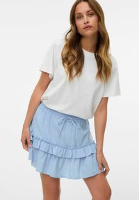 Jupe à volants superposés bleu clair avec une taille élastique et un cordon de serrage ajustable. Associée à un t-shirt blanc à manches courtes uni.