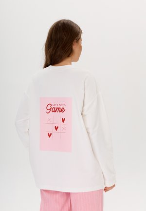 Witte sweatshirt met lange mouwen, voorzien van een roze rechthoekige graphic op de achterkant met de tekst "Laten we een spel spelen" en een tic-tac-toe ontwerp.
