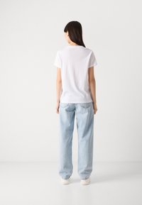 Vit bomullströja med rund halsringning, korta ärmar och avslappnad passform, tillsammans med ljusblå högmidjade jeans och vita sneakers.