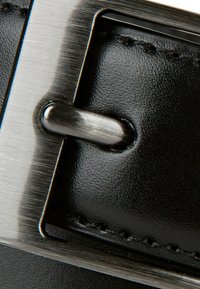 Czarny skórzany pasek z błyszczącą, szczotkowaną metalową klamrą; ma kwadratowy kształt, widoczne przeszycia oraz podkreślający srebrny ząb.