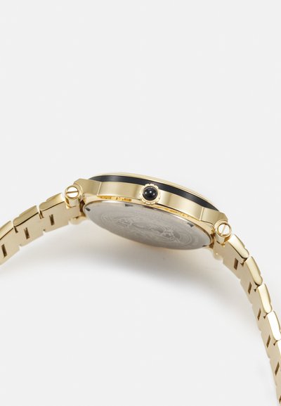 Gold wristwatch with a round case and black bezel. Metal band features rectangular links. The back displays intricate engravings and a crown.