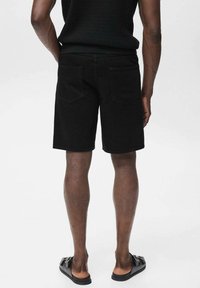 Zwarte denimshorts met een rechte snit, twee achterzakken en een gestructureerde tailleband. Draag ze met zwarte sandalen. Achteraanzicht.
