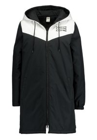 Lång svart och vit Vans-jacka med huva, hel dragkedja, dragsko, sidofickor och Vans-logotyp på bröstet.