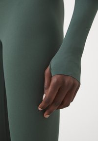 Grüner Langarm-Bodysuit mit einer weichen, glatten Textur. Verfügt über ein figurbetontes Design und Daumenlöcher an den Handgelenken für einen sicheren Sitz.