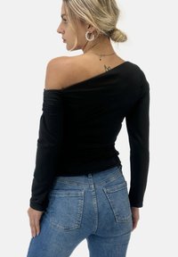 Zwarte off-the-shoulder langemouwen top met een gerimpelde textuur, gecombineerd met lichtblauwe high-waisted denim jeans met achterzakken.