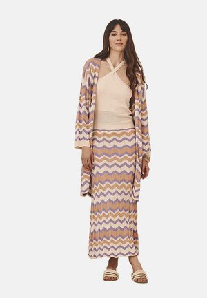 Conjunto de punto multicolor con un patrón de zigzag, que incluye una blusa sin mangas, una falda larga y un cárdigan abierto. Las zapatillas completan el look.