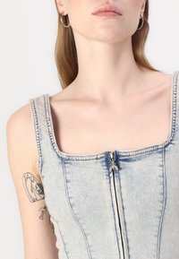 Top in denim blu chiaro con scollatura quadrata, cuciture visibili e dettaglio con zip centrale. Presenta spalline larghe e una vestibilità strutturata.