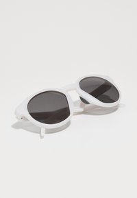 Gafas de sol octagonales blancas con lentes negros. Montura de plástico ligera, que presenta un diseño angular único y acentos laterales para mayor estabilidad.