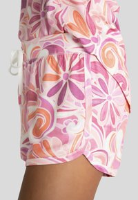 Roze korte broek met bloemenpatroon, gemaakt van zachte stof, met een koordtaille en een gebogen zoom, voorzien van oranje en paarse accenten.