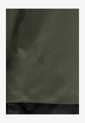 Olivi vihreä lyhythihainen paita, jossa on teksturoitu kangas, hienovarainen logo alahelmassa ja siistit ommellut reunat.