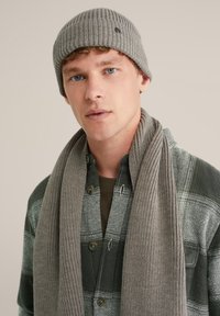 Beanie din tricot ribbed gri și fular asortat purtate peste o cămașă în carouri verzi și gri. Caracteristicile includ nasturi și o textură moale.