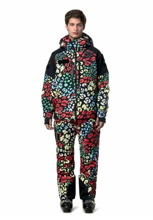 Giovane persona che indossa una giacca invernale colorata con stampa leopardata e pantaloni abbinati, in piedi di fronte con le mani rilassate ai lati.