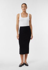 Jupe crayon noire en tricot avec une taille haute et une coupe longueur cheville, associée à un débardeur blanc et des chaussures plates noires. Texture lisse.