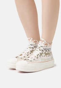 High-top sneakers in cream canvas with a patterned fabric upper, featuring metallic eyelets and textured rubber soles for grip.