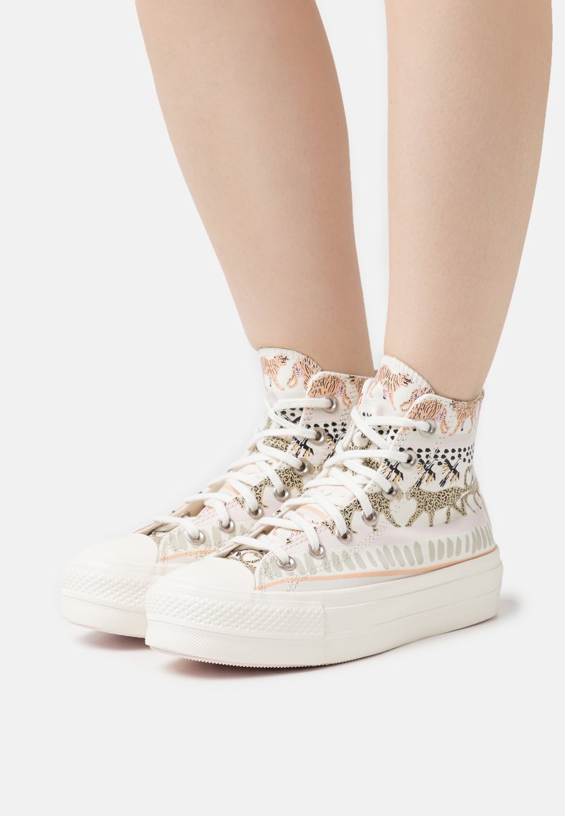 High-top sneakers in cream canvas with a patterned fabric upper, featuring metallic eyelets and textured rubber soles for grip.
