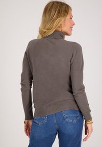 Grijze coltrui met een gladde textuur, aansluitend ontwerp en geribbelde onderrand, gecombineerd met blauwe jeans. Achteraanzicht.