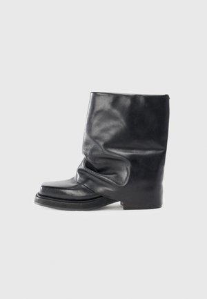 Stivale in pelle nera alla caviglia con design morbido, punta squadrata, tacco basso e texture liscia. Stile minimalista senza hardware visibili.