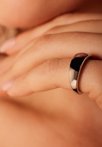 Silberner Bandring mit glatter, polierter Oberfläche, leicht abgerundeten Kanten, getragen an einem Finger vor einem natürlichen Hautton-Hintergrund.