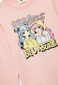 Różowy sweatshirt z dwiema ilustrowanymi postaciami o niebieskich i różowych włosach. Tekst w języku japońskim i angielskim: "Jesteś zbyt piękna."