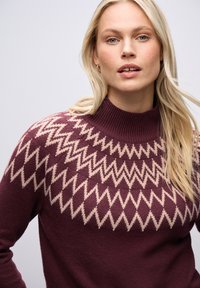 Burgundská vlněná svetr s vysokým žebrovaným límcem a smetanovým cik-cak vzorem přes hruď. Měkká textura, volný střih, všestranný design.