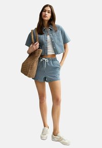 Conjunto de camisa de algodón de corte corto con mangas cortas a rayas azules y blancas y pantalones cortos, que cuenta con una cintura con cordón. Se complementa con una bolsa de mimbre y zapatillas.