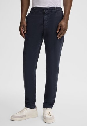 Navy blue chinos made from lightweight fabric, featuring a flat front, side pockets, and belt loops, paired with white sneakers.