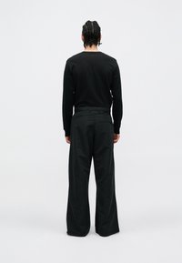 Maglietta nera a maniche lunghe e pantaloni a gamba larga, entrambi in un colore uniforme. Tessuto dalla texture liscia, vestibilità rilassata, design minimalista.