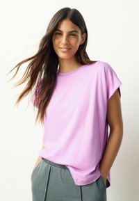 Hellviolettes Baumwoll-T-Shirt mit kurzen Ärmeln, legerer Passform, rundem Halsausschnitt und weicher Textur, kombiniert mit grauer Hose mit elastischem Bund.