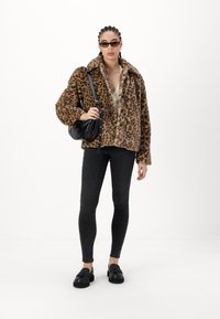 Jasje van nepbont met luipaardprint en een kraag, gecombineerd met een beige top, zwarte skinny jeans en zwarte instappers. Inclusief een kleine zwarte tas.