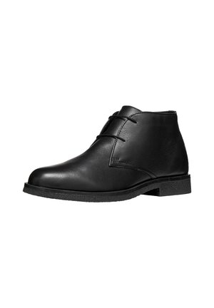 Bottine en cuir noir avec deux œillets et une semelle plate texturée, présentée sur fond blanc.