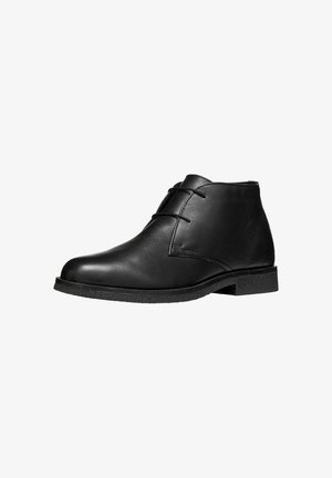 Bottine en cuir noir avec deux œillets et une semelle plate texturée, présentée sur fond blanc.