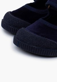 Zapatillas de lona azul marino con suelas de goma texturizada y punteras redondeadas, que presentan un ligero brillo y detalles de costura en contraste.