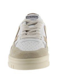Baskets blanches et beiges avec une tige en daim et en cuir, perforations texturées sur le bout, lacets ronds et semelle en caoutchouc beige.