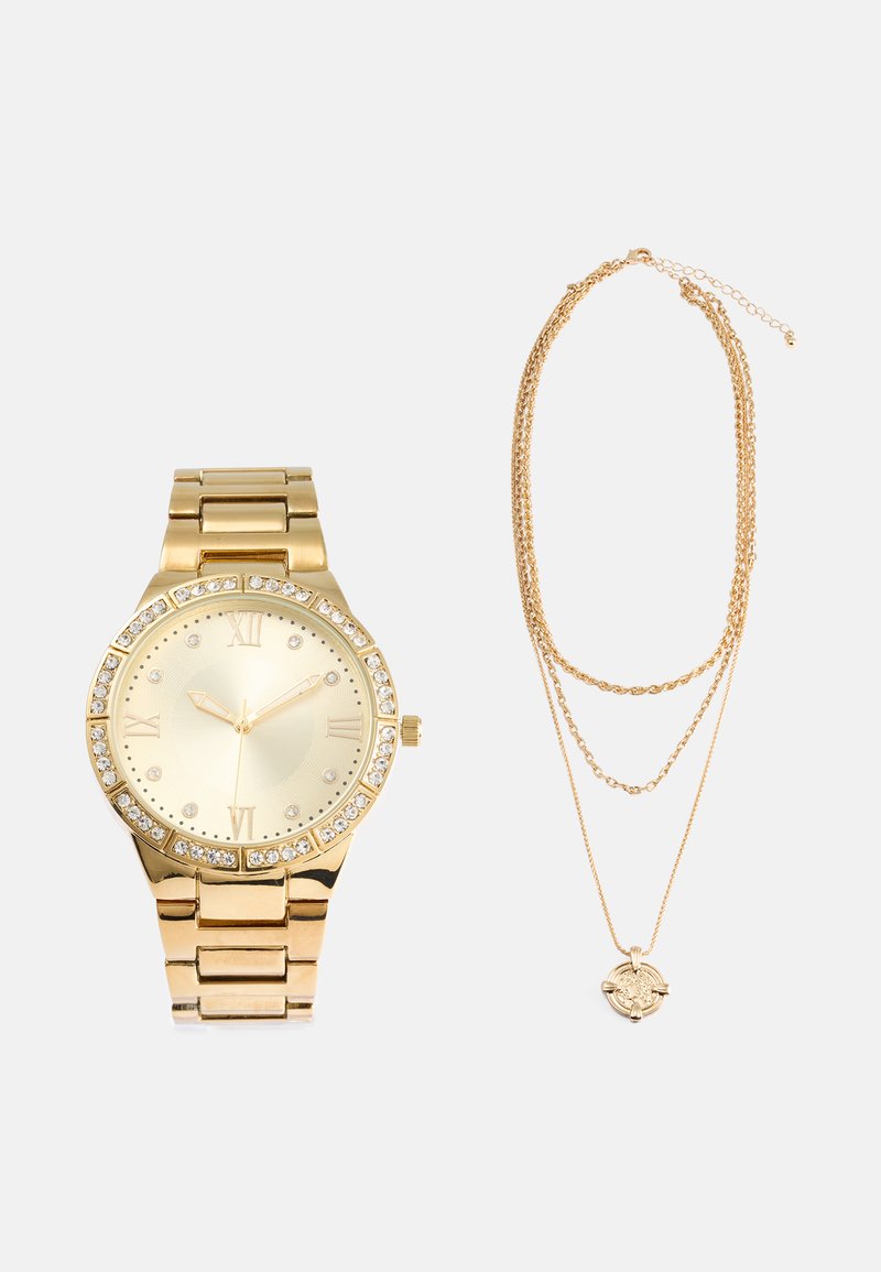 Relógio de tom dourado com números romanos, detalhes em cristal no bisel, bracelete ligado. Colar em camadas de tom dourado com detalhe de pendente.