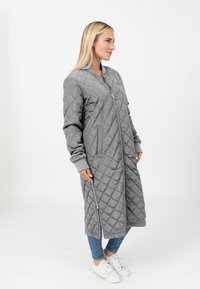 Gequilted grijze lange jas met een ritssluiting aan de voorkant, geribde manchetten en zijzakken. Heeft een ruitpatroon textuur en een relaxte fit.