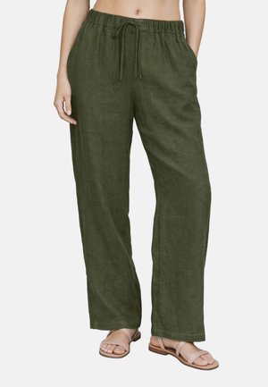 Donna che indossa pantaloni larghi in lino verde oliva con elastico in vita e coulisse, abbinati a sandali piatti beige.