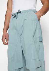 Ljusblå cargobyxor i bomullsmaterial. Har elastisk midja med dragsko, sidofickor och förstärkta sömmar.