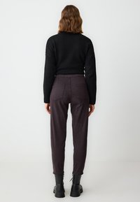Zwarte gebreide trui, donkergrijze cropped pants met elastische tailleband, twee achterzakken en zwarte enkelboots met dikke zolen.