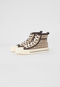 Hoge sneakers gemaakt van canvas in een beige kleur met een bruin grafisch patroon. Voorzien van witte veters en een geëtste crème rubberen zool.