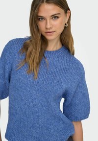 Modrý pletený svetr s kulatým výstřihem, krátkými rukávy a volným střihem; vyznačuje se texturovanou tkaninou a měkkým, uvolněným vzhledem.