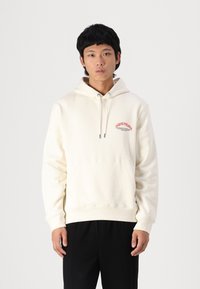 Haut de sweatshirt beige clair avec poche kangourou, capuche à cordon et impression graphique rouge. Fabriqué en tissu doux, avec des poignets et un ourlet côtelés.