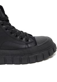 Mustad mustad sneakerid on valmistatud nahast ülemusest, kummist varbakaitsest, tekstureeritud tallast ja mustadest paeladest, nähtavate õmblustega ning tükkilisest disainist.
