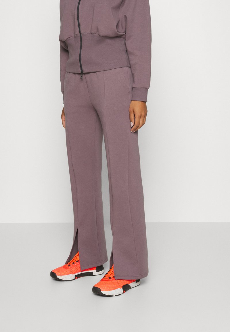 Helllila Sweatpants mit lockerer Passform und seitlichen Schlitzen am Saum, kombiniert mit leuchtend orangefarbenen Sportschuhen mit schwarzem Sohlen.