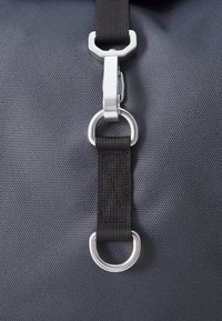 Borsa in tessuto nero con superficie testurizzata, dotata di clip in metallo argentato e di un anello in metallo sovradimensionato attaccato a una tracolla intrecciata.