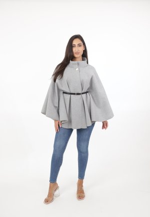 Grå ullkappa med hög krage, framknäppning och ett svart bälte i midjan, lagd över blå skinny jeans och genomskinliga klackar.