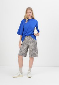 Királykék, oversized, rövid ujjú ing, mintás szürke leopárd mintás rövidnadrág, bézs sportcipő és világos színű zoknik. Egyszerű dizájn, laza szabás.